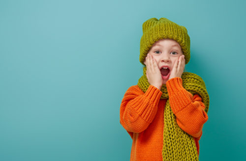 Winter portrait of happy child wearing knitted hat, snood and sweater. Girl having fun, playing and laughing on teal background. Fashion concept.