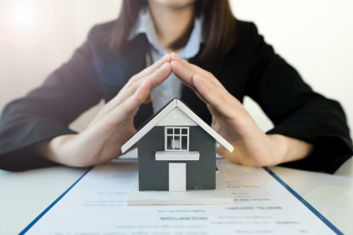 The hand of a home insurance broker protecting the small home on the desk.