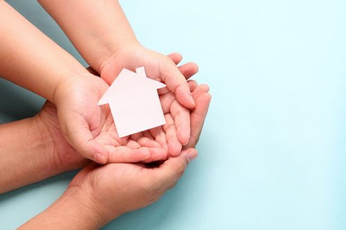 hands holding paper house on blue background.